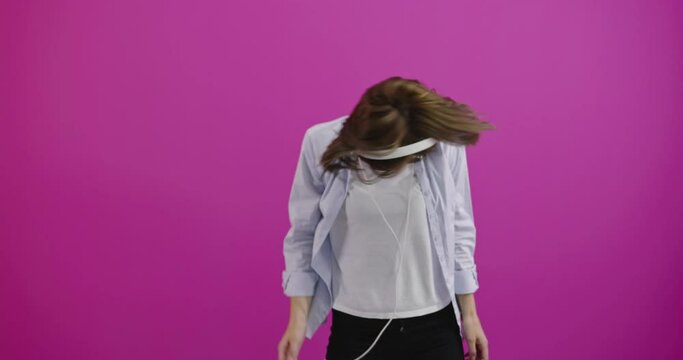 Happy woman or teenage girl in headphones listening to music from smartphone and dancing over color background