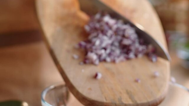 Rack focused tit down shot of hands of male cook putting chopped red onion from wooden cutting board into glass bowl