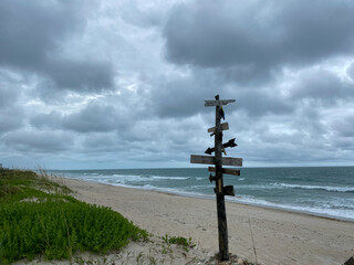 A city directional sign at a beach showing how far cities are from this point on a beach