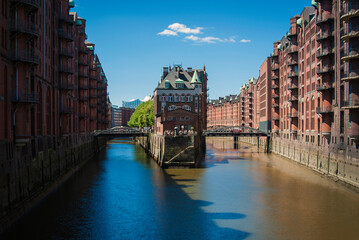 Cityscape, Speicherstadt, Hamburg, Germany. Canal with water, on both sides - houses made of brown bricks. Two bridges in the center of the frame. 