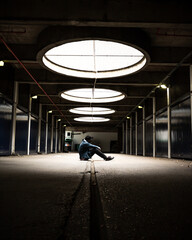 A man sitting in a parking garage under a bright spotlight