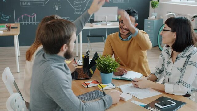 Male and female coworkers are doing high-five sharing ideas working together in office. Cooperation, young people and modern business concept.