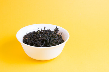 mixed black tea in little white bowl on a yellow background, copy space