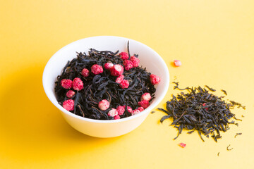 a bunch of tea with dried strawberries in a small white bowl on a yellow background, a handful of tea is scattered on a yellow background