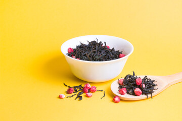 tea with dried strawberries in a white bowl, strawberry tea in a large wooden spoon on a yellow background, copy space, sprinkled berries and dried tea leaves