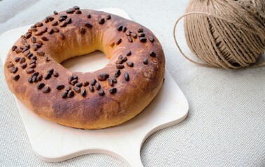 Composition on gray linen fabric: homemade crunchy bagel with pine nuts on a wooden board, packing cord reel nearby (upper right corner)