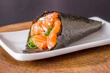 Salmon temaki sushi on white plate in black background