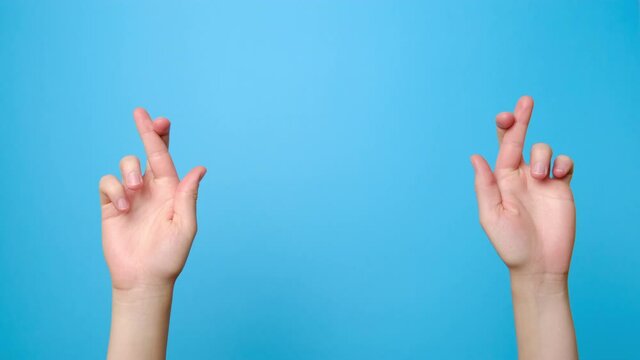 Close up of female hands praying with crossed fingers hopes for miracle good outcome, isolated on blue studio background with copy space. Body language concept. Advertising area, workspace mock up