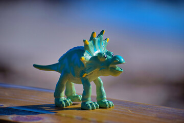 Dinosaur toy standing outside with the beach and ocean in the background. © CarlyZel