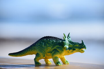 Dinosaur toy standing outside with the beach and ocean in the background. © CarlyZel