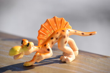 Dinosaur toy standing outside with the beach and ocean in the background. © CarlyZel