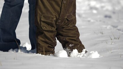 Detail of baby child feet walk in snow, first steps, parent support child, learning process in winter park, together no matter the times