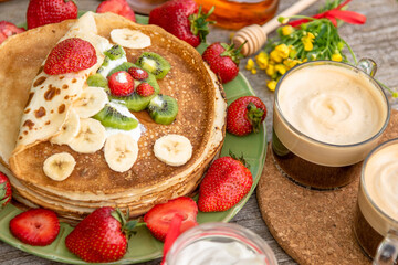 Pancakes with strawberries, kiwi, bananas and two cups of coffee for Breakfast. Bear of fruit and berries on pancakes.