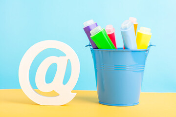 A metal bucket with highlighter marker pen and at symbol or commercial at on a blue background. Back to school