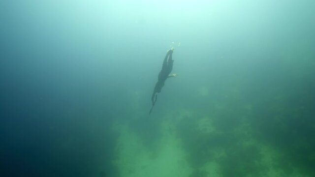 Full length of shirtless man spearfishing while swimming over ocean floor in sea - Wakatobi Regency, Indonesia