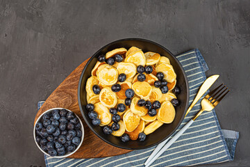 Trendy home breakfast with tiny pancakes and blueberry on gray concrete background. Flat lay, top view, overhead, mockup, template, copy space. View from above. High quality photo