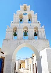 A narrow cobblestone street with an arched bell tower in the traditional village of Megalochori in Santorini, Greece.
