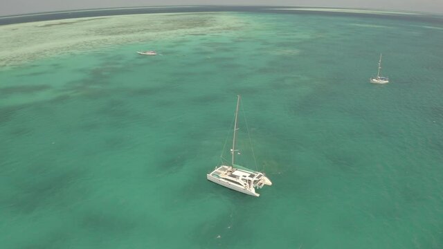 Aerial shot of boats moored on turquoise sea against sky, drone ascending backward over vessels on sunny day - Wakatobi Regency, Indonesia