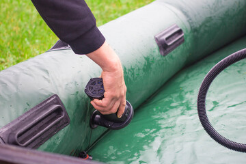 Man outdoors in nature inflating green rubber boat. Preparing for outdoor camping and fishing trip on a summer day