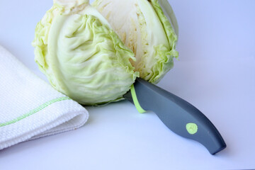 Fresh white cabbage is cut in half with a knife.
Close-up, horizontal photo. There is a place for...