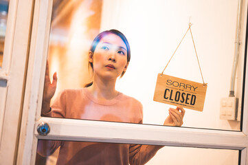 Asian woman store owner turning hanging closed sign in front door of her shop