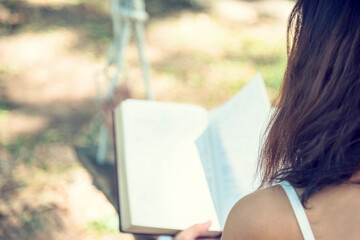 Obraz premium Relax woman holgind bible book read outdoors sitting on green garden in park. Young woman relaxation reading open book in autumn fall season at home garden. Smart beautiful woman lifestyle learner.