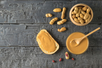 Bread with peanut paste and peanuts on a black wooden table.