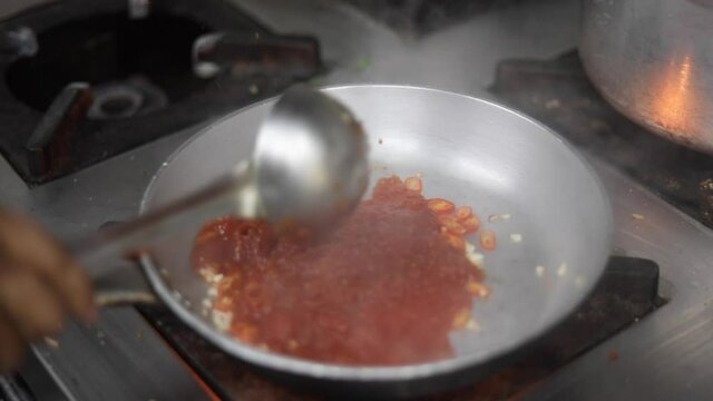 Cooking red sauce, with sauteed vegetables, caramelised onions, red chillies and capsicum on a hot oil pan.