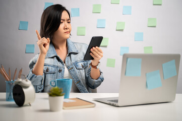 Asian woman looking at smart phone reading news and feel confused at home office. WFH. Work from home. Prevention Coronavirus COVID-19 concept.