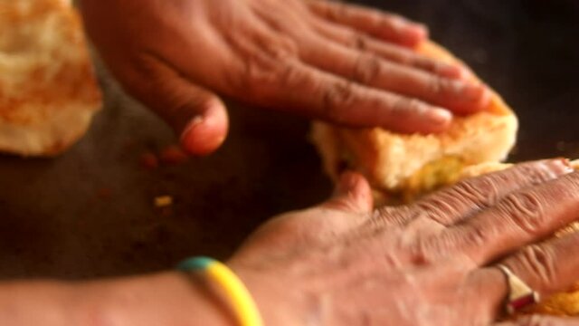 Making indian street vada pav on a fry pan served with green chutney, red tomato sauce and masala.