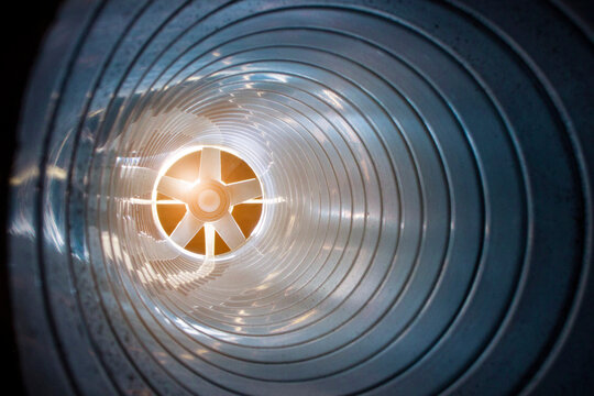 Closeup View From Inside The Galvanized Steel Air Duct On The Exhaust Fan In The Background Light, The Front And Back Background Is Blurred With A Bokeh Effect