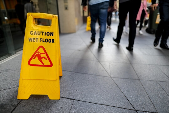 Safety workplace caution wet floor warning sign on the floor surfaces with defocused people walking at the background 