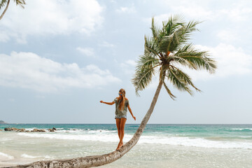 Obraz premium Young lady tourist walking along tropical sandy beach with palm trees. Happy girl walking on the palm tree with ocean view. Summer concept