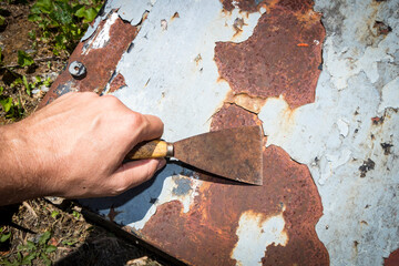 Man's hand removing paint and rust damage from metal doors using a metal paint scraper
