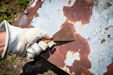 Man's hand removing paint and rust damage from metal doors using a metal paint scraper - obrazy, fototapety, plakaty