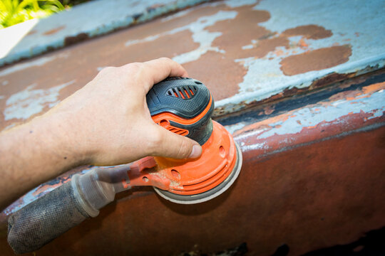 Man's hand operates a disc/orbital sander, to remove paint and rust from metal doors