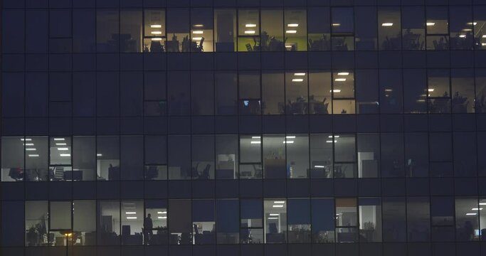 Late working over hours people in the corporate building, offices lights seen from outdoor