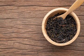 Chinese leaf tea in a wood bowl on grained wood background