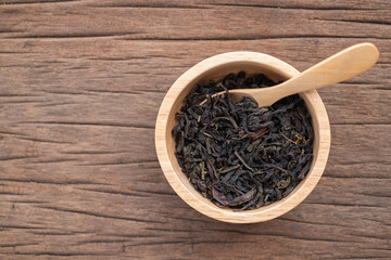 Chinese leaf tea in a wood bowl on grained wood background
