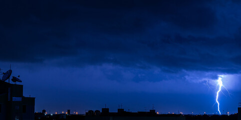 Copy space of severely lightning thundering down at the night with silhouette of building.