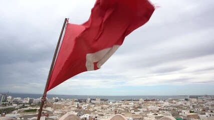 Closeup view of red Tunisian flag standing on roof of high building isolated at aerial view cityscape background.