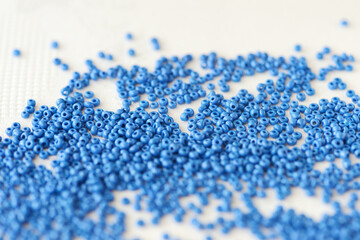 Seed beads blue color scattered on a textile background close-up. Handmade, art, creativity