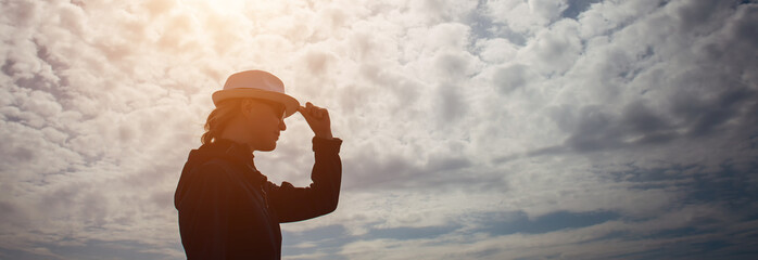 Female silhouette in profile with hat in hand against the mysterious sky with clouds. Outline of...
