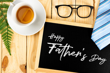 Happy Father Day background concept with blue necktie, glasses, cup of tea and blackboard on wooden background with copy space for text.