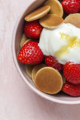 Homemade cereals mini pancake with yogurt, honey and strawberries on colorful background.
