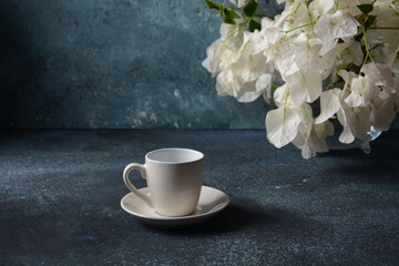 Composition with white cup of coffee , beans  and flowers as background