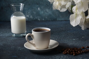 Composition with white cup of coffee , beans  and flowers as background