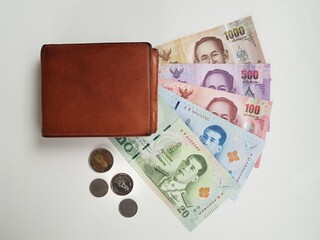 Brown leather wallet with current Thai baht banknotes and coins on white background.