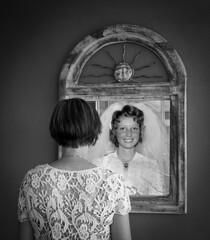 Woman looking at reflection in mirror, image is composite of same woman, older and younger