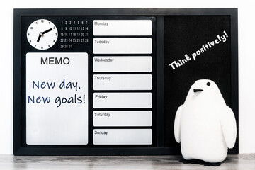 Motivational concept, the concept of success. On a blackboard for reminders with a clock, calendar, and days of the week, it says: "New day, new goals!"